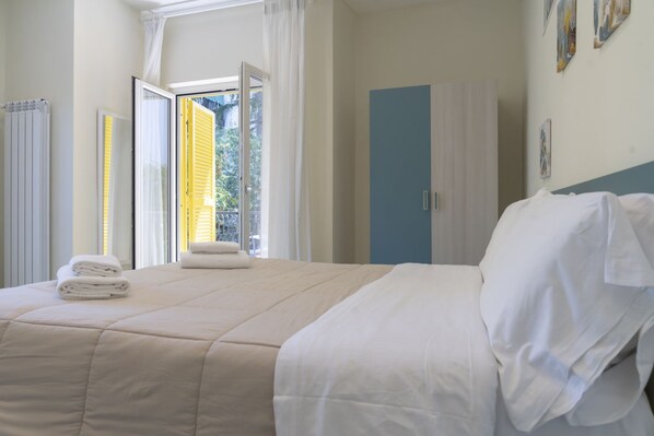 A neatly made bed with white linens, a blue wardrobe, and a window with curtains.
