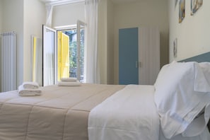 A neatly made bed with white linens, a blue wardrobe, and a window with curtains.