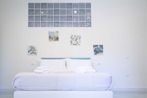 Une chambre d’hôtel avec un grand lit, du linge de lit blanc et quatre œuvres d’art accrochées au mur.