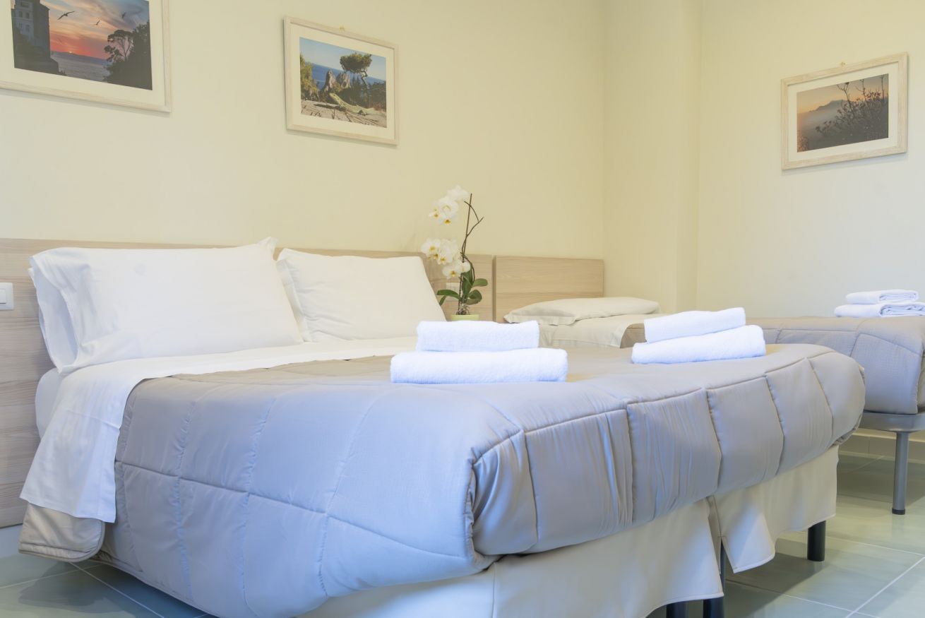 Una camera d'albergo con due letti, biancheria bianca, un tavolino con un vaso di fiori e quadri appesi alle pareti.