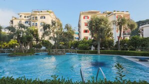 A swimming pool surrounded by lush greenery and modern buildings with balconies. - Modern Apartment with Terrace, Swimming Pool&Tennis (Sorrento)