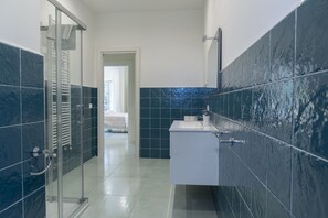 A modern bathroom with a glass shower enclosure, a white sink, and blue-tiled walls.
