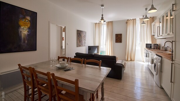 A modern kitchen with a dining area, wooden chairs, a table, and a TV in the background. - Pauillac two bedroom apartment on second floor (Blaye)