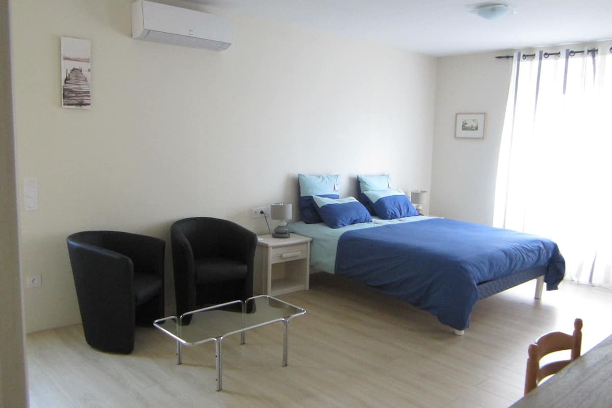 A bedroom with a bed, a chair, a small table, and a nightstand.