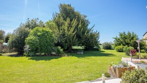 A well-maintained garden with a variety of trees and shrubs, a clear sky, and a stone pathway leading to a wooden pergola. - Les Cagouilles (Virson)