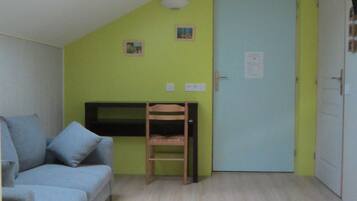 Una habitación con techo inclinado, una cama, una silla, una puerta y un aire acondicionado instalado en la pared.