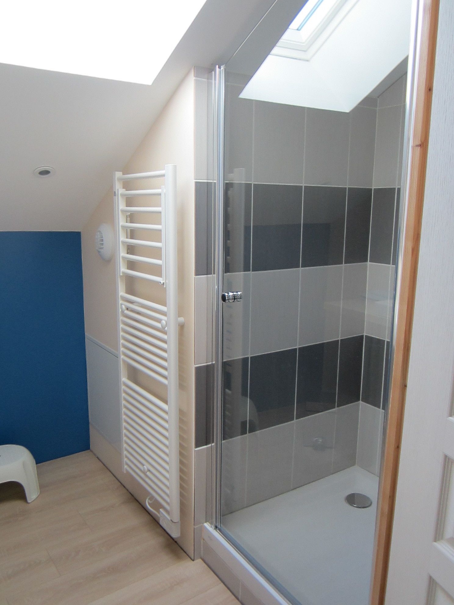 Een douche met een glazen deur, een witte handdoekhouder en een blauwe muur.