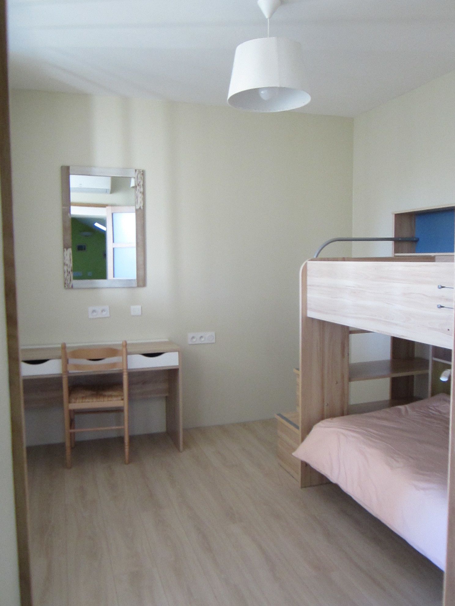 A bunk bed room with a desk and chair, a mirror, and a hanging light fixture.