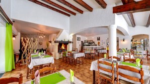 Un restaurant aux poutres apparentes, aux murs de pierre et doté d’une cheminée. Les tables sont dressées avec des sets de table verts et des nappes blanches.
