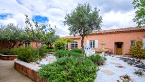 Une cour avec une fontaine, un bâtiment doté d’un toit en tuiles et diverses plantes.