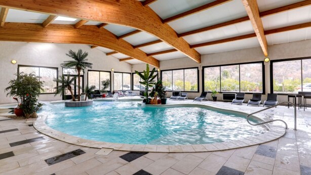 Une piscine intérieure avec un sol carrelé, des poutres en bois et des chaises longues disposées autour de la piscine.