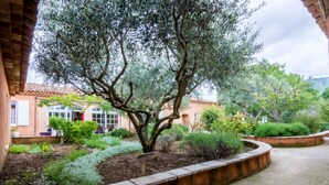 Un jardin avec un grand arbre, un mur en briques et un bâtiment doté d’un toit en tuiles.