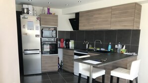 A modern kitchen with a refrigerator, oven, microwave, and a bar area with stools. - RENTED VILLA F3 RENTED IN THE GREEN AREA (Sainte-Maxime)