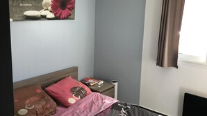 A bedroom with a bed, pillows, a nightstand, a wall art, and a window with curtains. - RENTED VILLA F3 RENTED IN THE GREEN AREA (Sainte-Maxime)