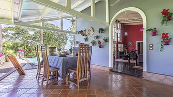 A covered patio area with a table and chairs, surrounded by potted plants and a view of the outdoors.