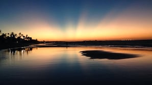 Praia ao pôr do sol, com águas calmas e silhuetas de palmeiras.