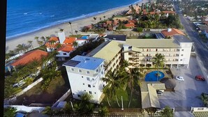 Vista aérea de um hotel à beira-mar, com vários edifícios, uma piscina e uma praia.