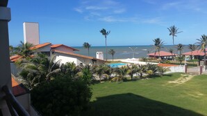 Vista de uma propriedade à beira-mar com piscina, palmeiras e um edifício com telhado vermelho.