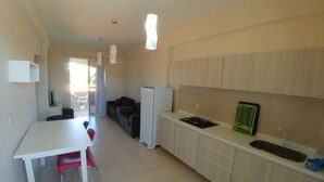 Uma cozinha compacta com uma mesa e cadeiras brancas, geladeira, fogão e pia.