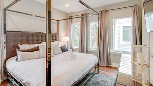 Ein Bett mit Baldachin und einem gepolsterten Kopfteil, ein Nachttisch mit Lampe sowie ein Blick ins Freie durch ein Fenster mit Vorhängen.