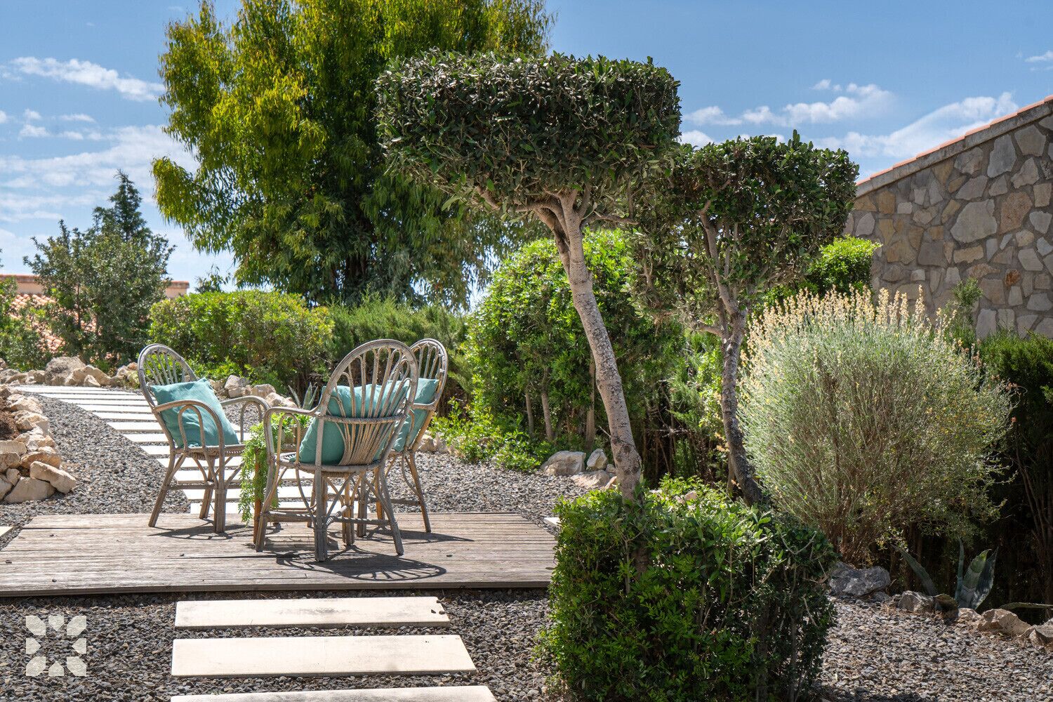 Une terrasse avec deux fauteuils en osier et une table, entourée d’un mur de pierre et de diverses plantes.