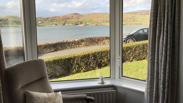 Una habitación con un amplio ventanal con vistas a un lago y colinas, una silla y un radiador.