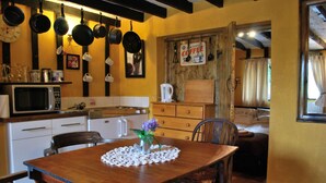 Una cocina acogedora con una mesa de madera, sillas y un microondas. Hay ollas colgadas en la pared y un letrero que dice 'Coffee'.