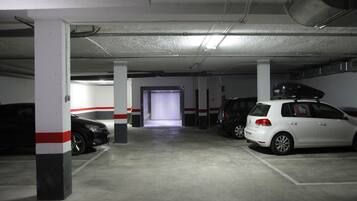 A parking garage with concrete pillars, a white car with a Hello Kitty decal, and a black car parked in the distance.