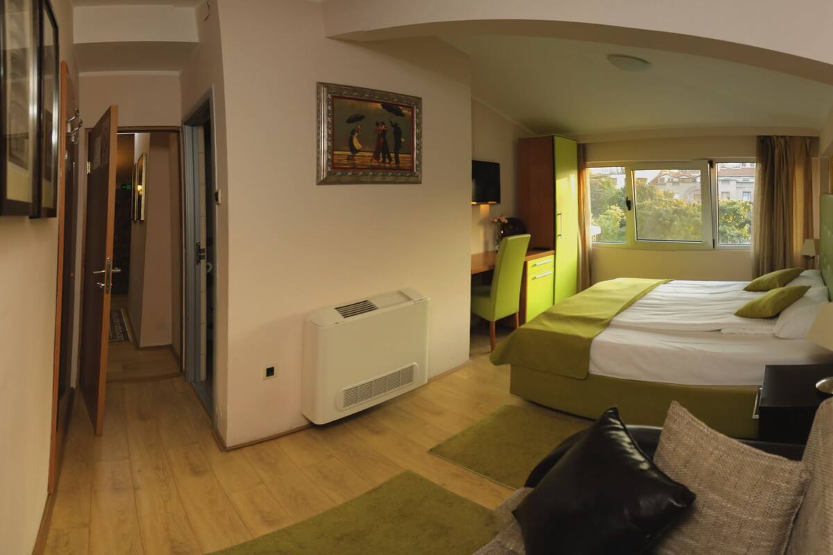 A hotel room with a bed, a desk, a chair, a window, and a door.
