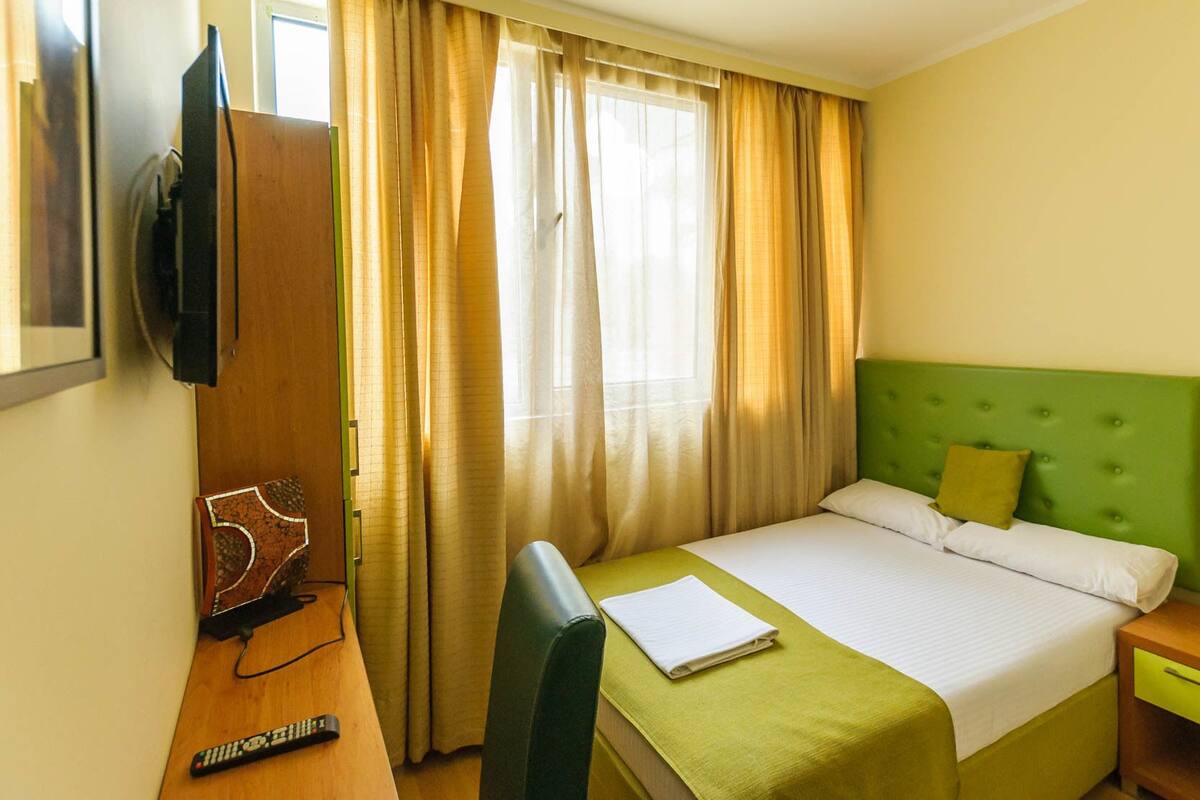 A hotel room with a bed, a desk, a chair, a television, and curtains.