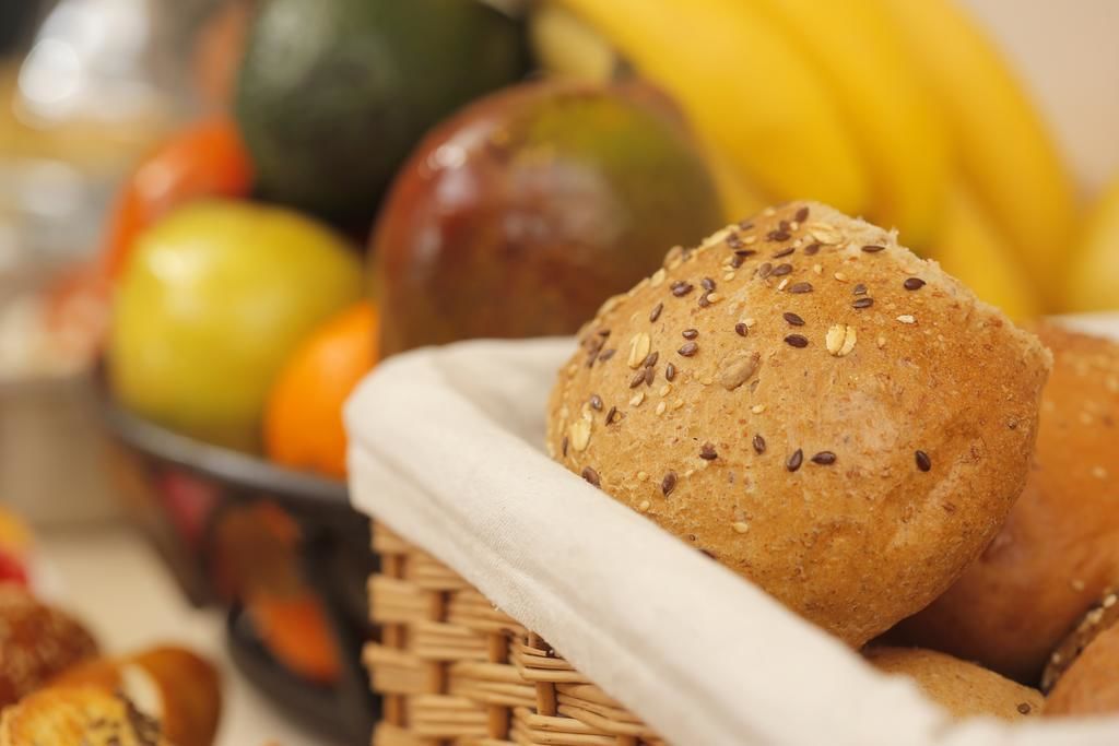Un panier rempli de petits pains aux graines, entouré de fruits comme des pommes et des bananes.