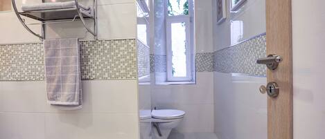 A bathroom with a tiled backsplash, a toilet, a towel rack with a folded towel, and a door with a lock.