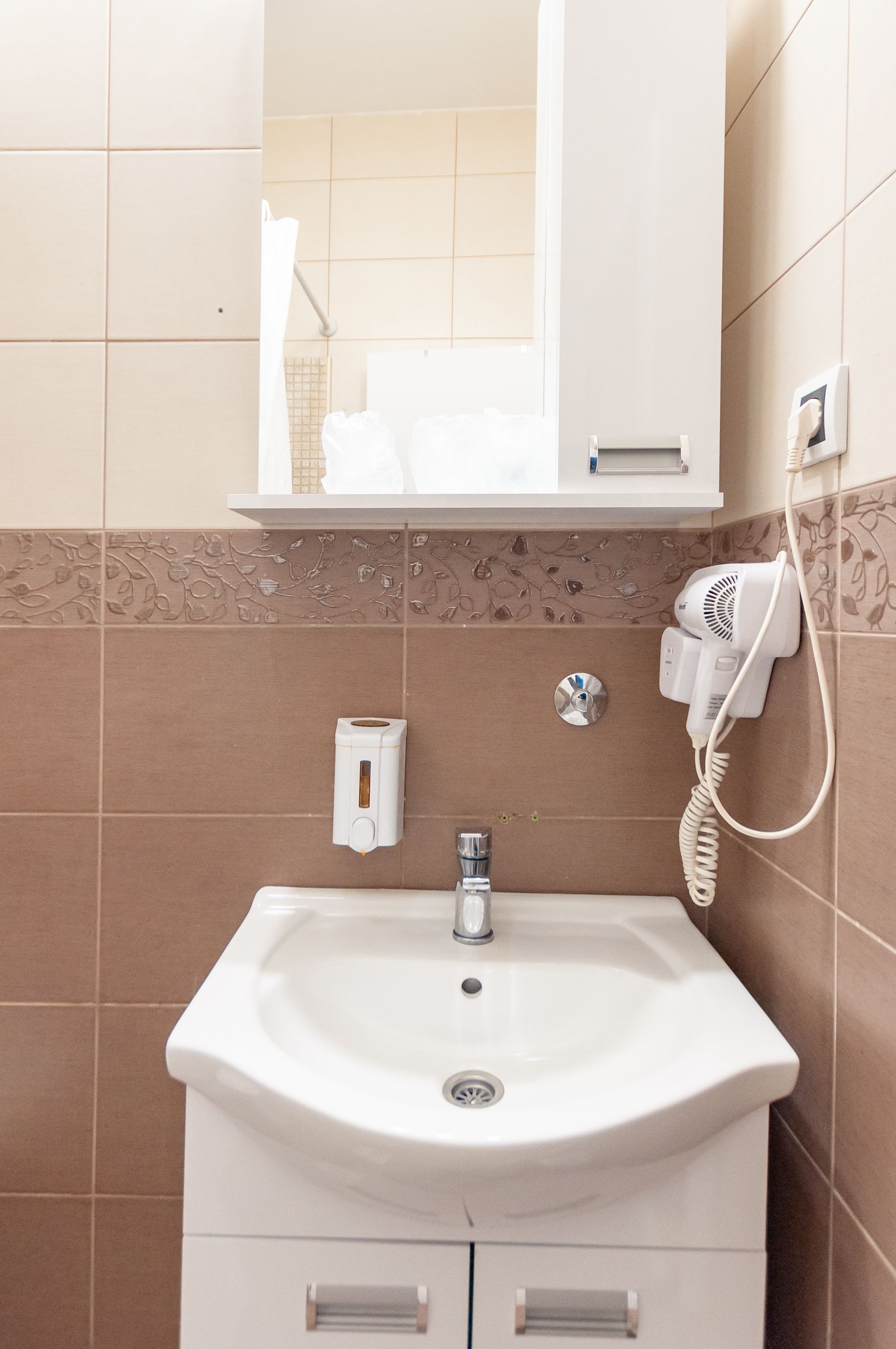 A bathroom with a white sink, a mirror, a towel rack, a hairdryer, and a soap dispenser.