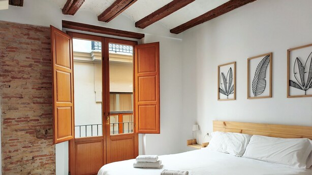 A bedroom with a large bed, wooden wardrobe, and a balcony with a view.