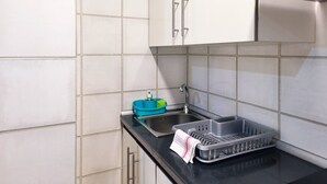 Une cuisine avec des carreaux blancs, des armoires en acier inoxydable, un plan de travail noir, un évier et un égouttoir à vaisselle.