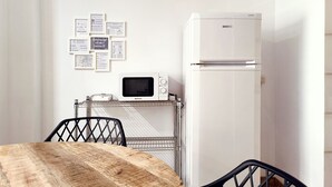 Une petite cuisine équipée avec un réfrigérateur blanc, un four à micro-ondes et un petit évier. Des cartes de bienvenue et des informations sont affichées dans des cadres au mur.