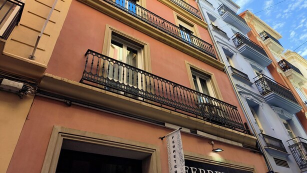 Un immeuble à plusieurs étages doté de balcons, dont la devanture est bien visible, et un ciel dégagé.