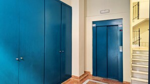 Un couloir avec deux portes bleues, un luminaire et un escalier muni d’une main courante.