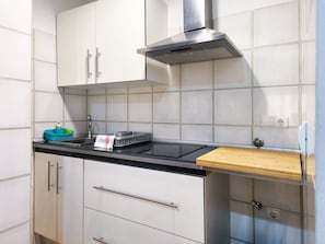 Una cocina moderna con armarios blancos, campana extractora de acero inoxidable, encimera negra y tabla de cortar de madera.