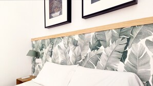 Un lit avec une tête de lit ornée d’un motif de feuilles, une lampe de chevet et un tableau encadré accroché au mur.