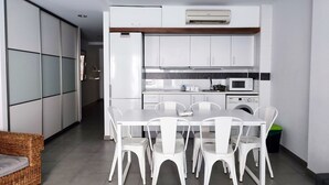A modern kitchen with white cabinets, a dining table with white chairs, and a wicker sofa.