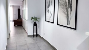 A hallway with framed botanical prints on the walls, a potted plant, and a sofa in the background.