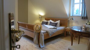 A bedroom with a sloped ceiling, a wooden bed with pillows labeled "Lounge Club," a bedside table with a lamp, and a window with curtains.