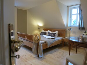 Quarto com teto inclinado, cama de madeira com almofadas com a etiqueta 'Lounge Club', mesa de cabeceira com abajur e janela com cortinas.