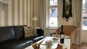A living room with a striped wall, a black leather sofa, a white table with a bottle of wine, glasses, and a wooden decorative piece.