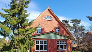 A red brick house with a green roof and white trim, surrounded by trees.