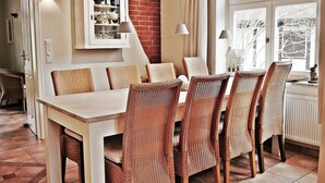 A dining area with wicker chairs and a white table, a cabinet with glass doors, and a view of a brick wall and window.