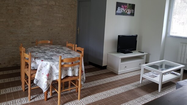 Ein Zimmer mit Esstisch, Stühlen, einem Fernseher auf einem Schrank, einem Glastisch und einem Fenster mit Jalousien.