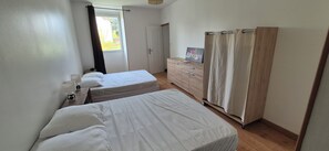 Une chambre d’hôtel avec deux lits simples, une commode en bois, un miroir et une fenêtre avec des rideaux.