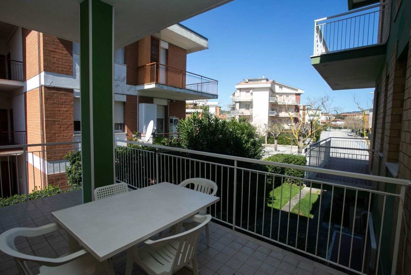 Een balkon met een tafel en stoelen, een uitzicht op omliggende gebouwen en een heldere lucht.